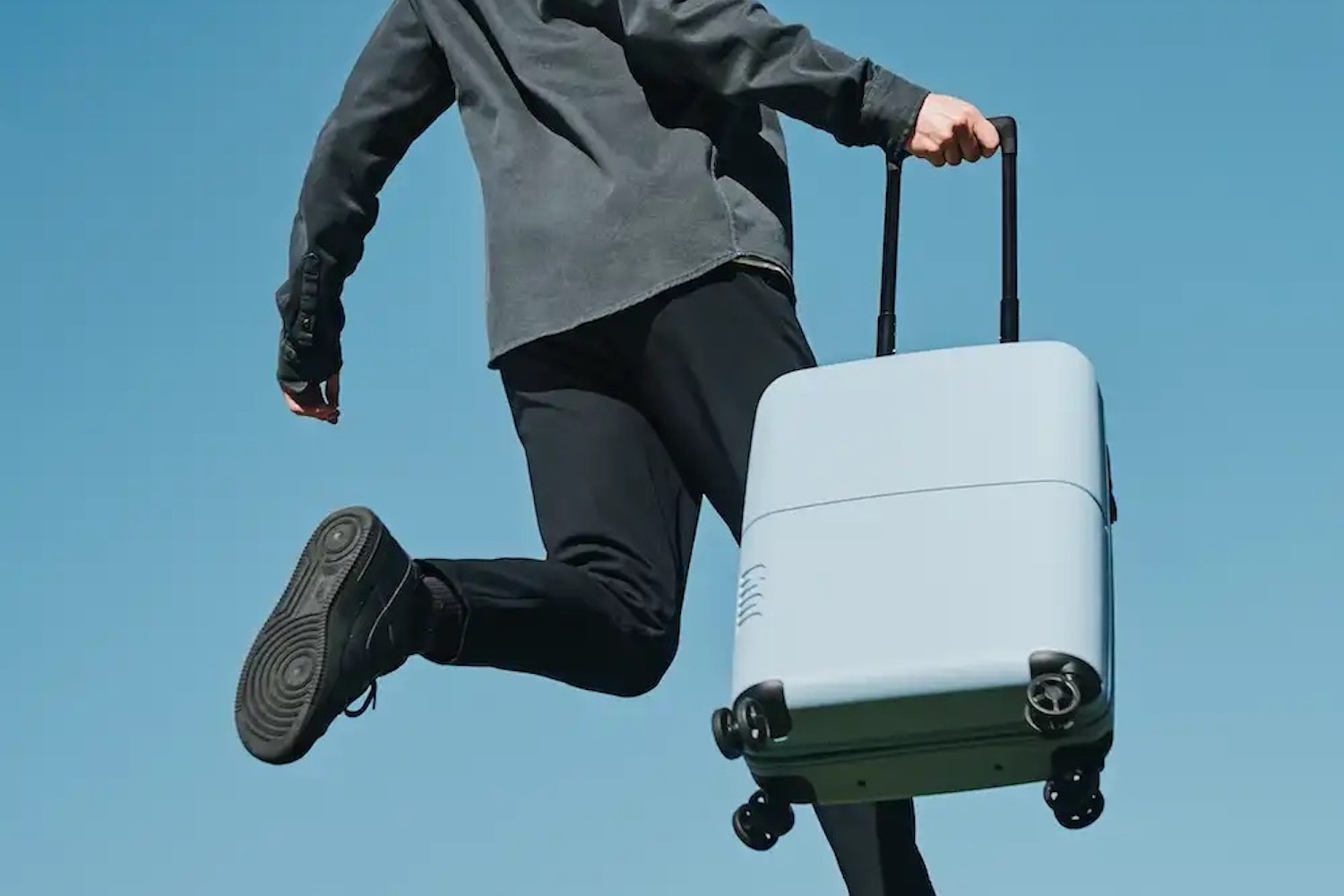 a model running with a blue July carry-on suitcase