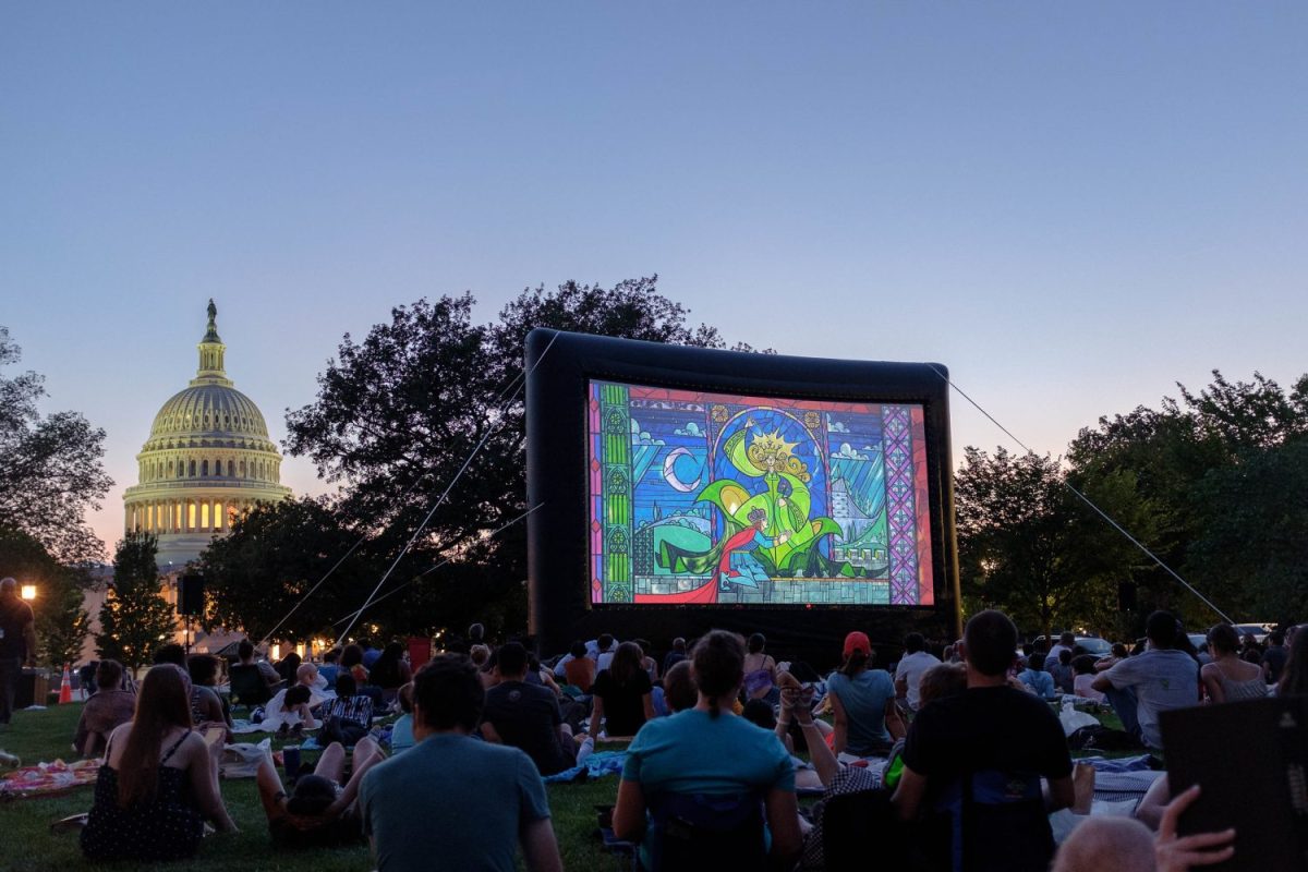 Capitol Hill behind projector screen showing movie on a lawn with people watching in Washington, D.C.
