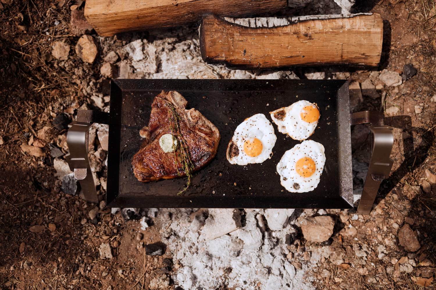 a Made In Griddle System with eggs and bacon over an open flame outside