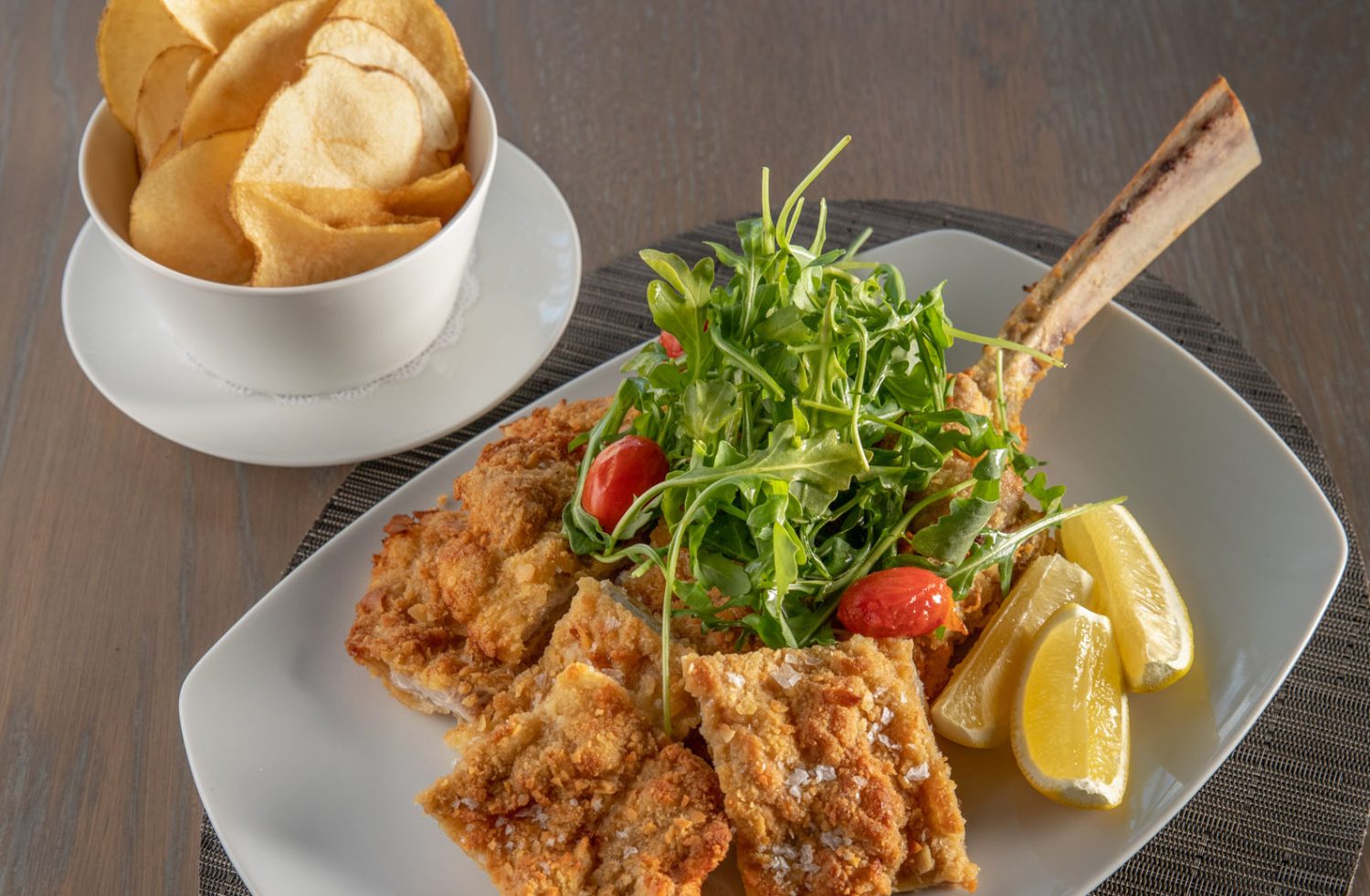 Plated veal, salad and potato chips.