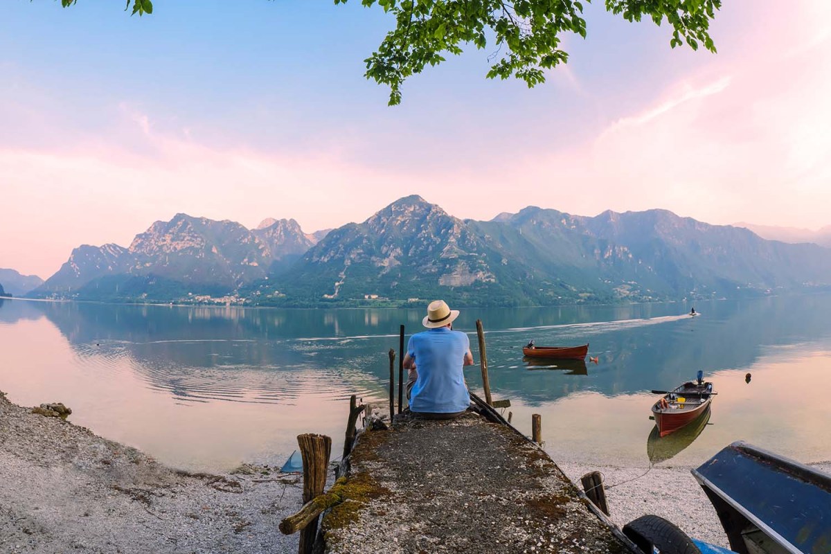 View of solo traveler sitting on jetty at Lake Idro at morning twilight