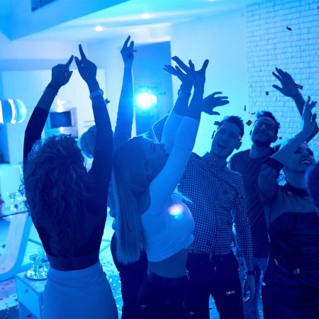 Group of modern young people dancing under confetti at private house party lit by blue light. Airbnb has announced an anti-party crackdown for Memorial Day.