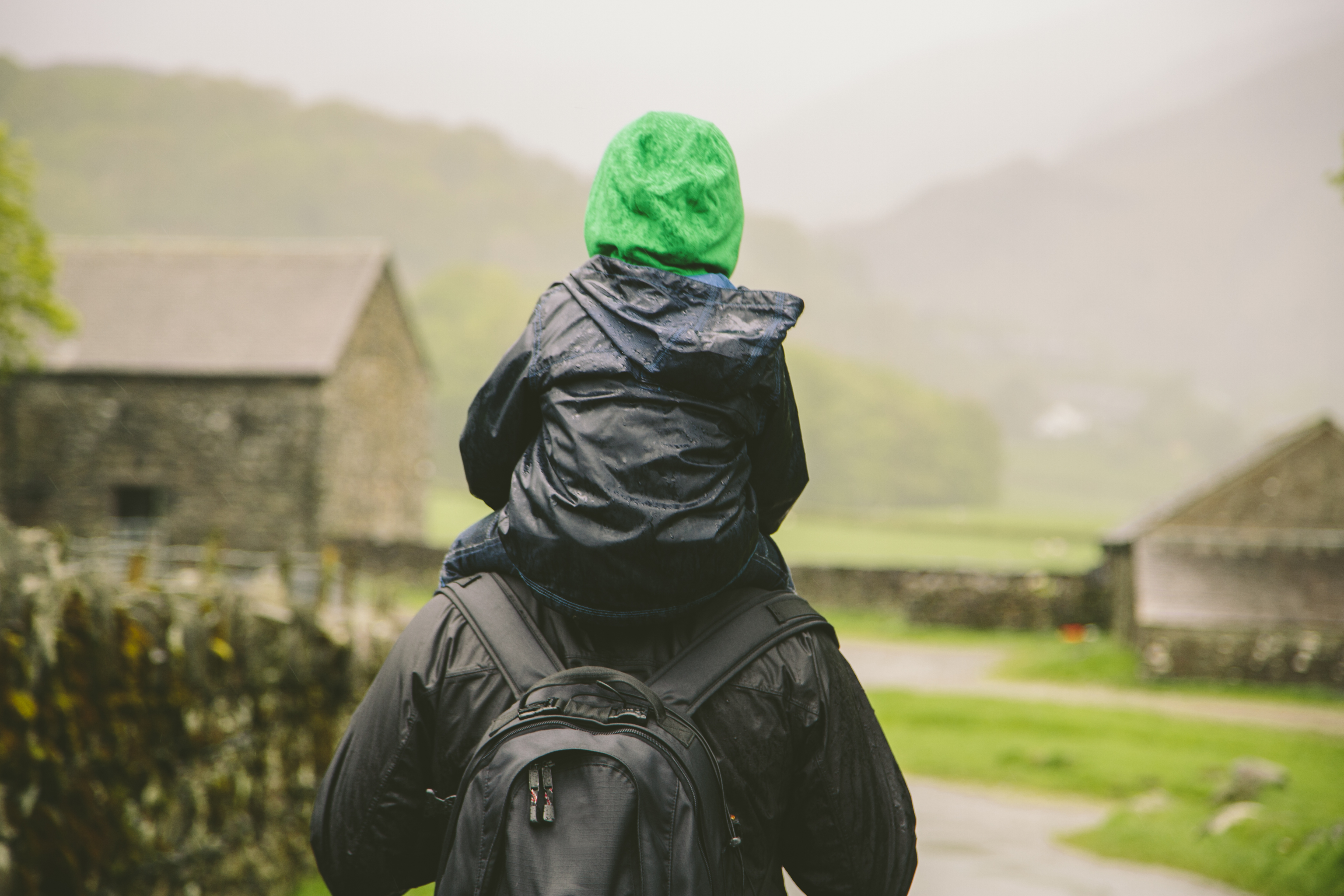 A kid sitting on his dad's shoulders outside on a walk.