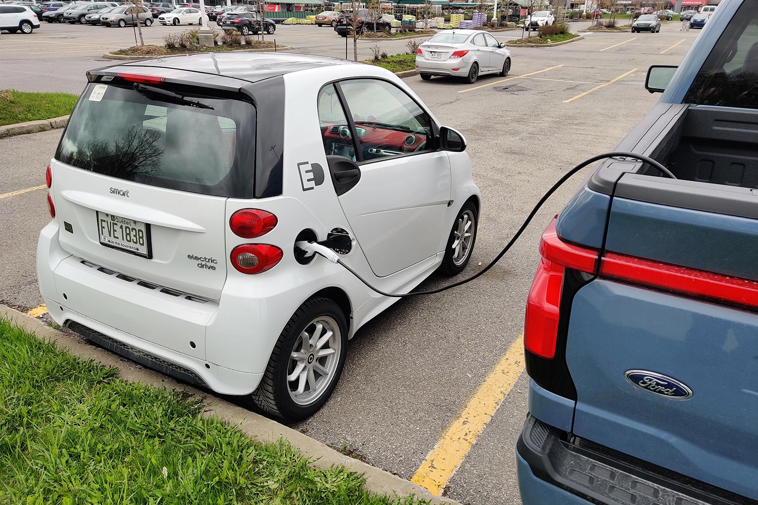 An electric Smart Fortwo car being charged by a Ford F-150 Lightning through vehicle-to-vehicle charging