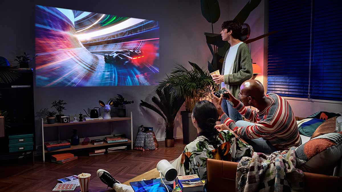 The Freestyle by Samsung in a living room where three people are playing video games. The Discover Samsung Event features discounts across the tech brand's portfolio.