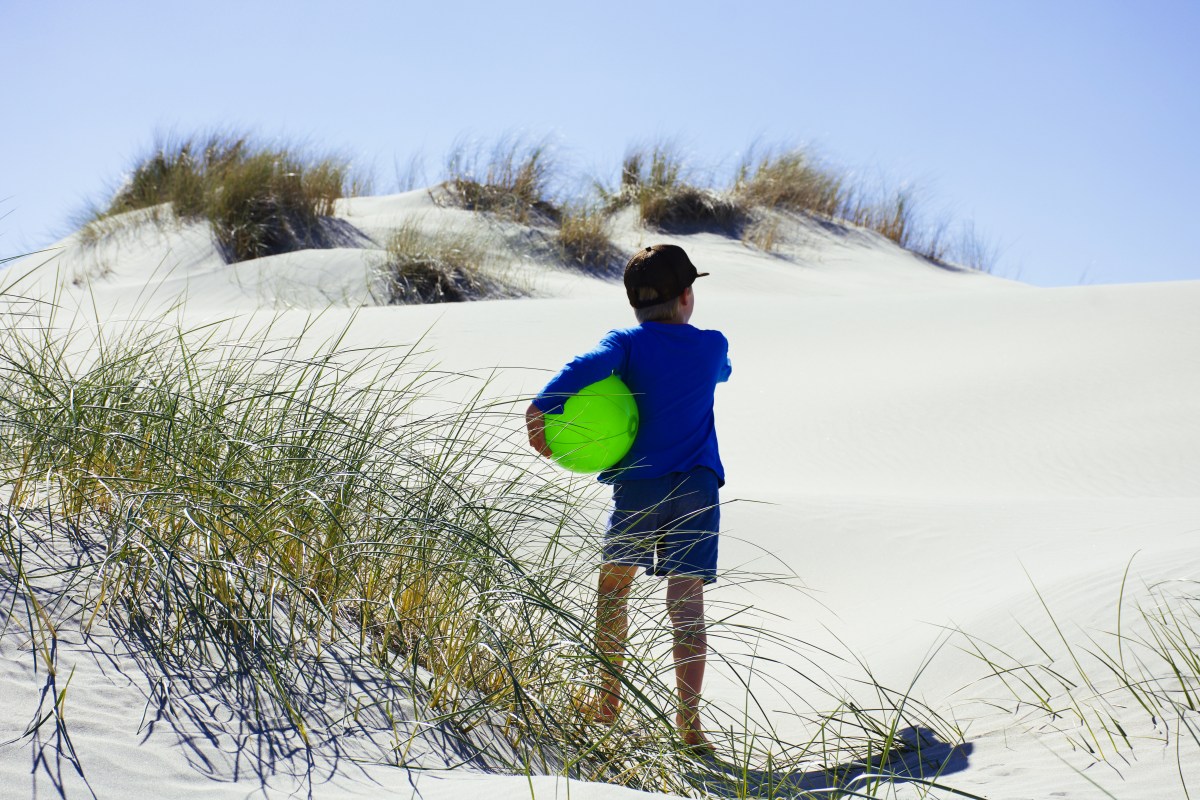 Child playing in sand dunes in an summer beach scene landscape.