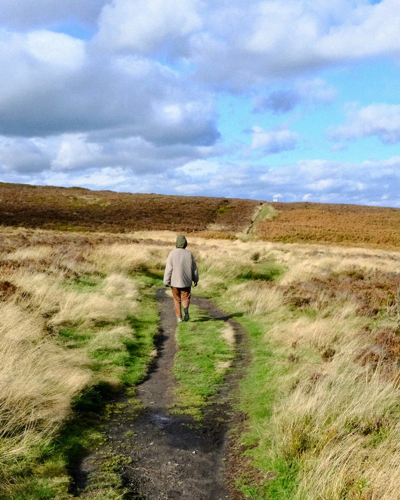 A man walking down a country lane with clouds above.