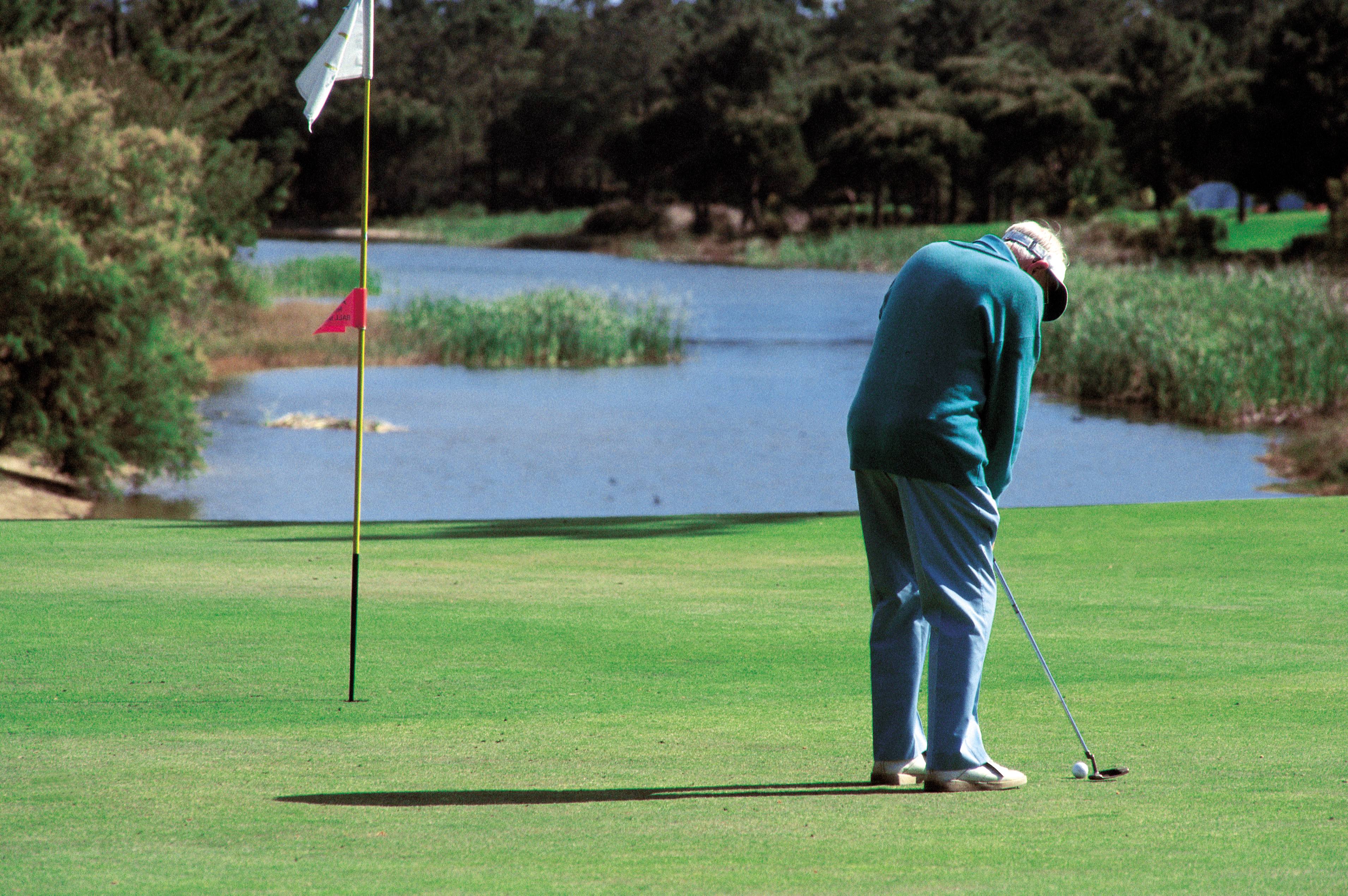 An old man putting on a golf green.