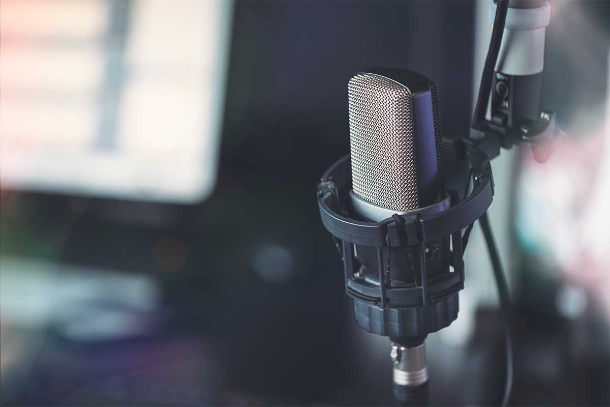 Close up of microphone in radio broadcast studio and computer screens on the background. Some podcasts are starting to use AI to write scripts and even host.