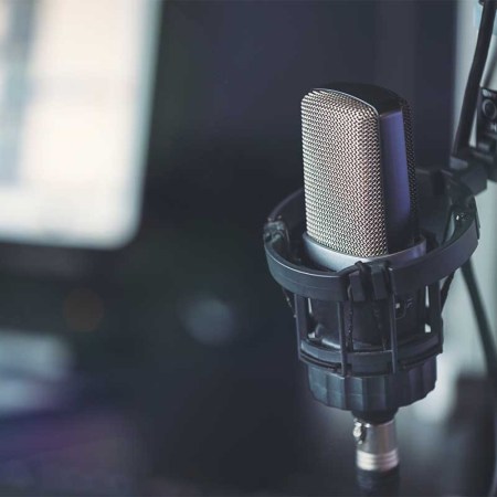 Close up of microphone in radio broadcast studio and computer screens on the background. Some podcasts are starting to use AI to write scripts and even host.