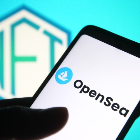 OpenSea logo on a smartphone, with the word NFT in the background