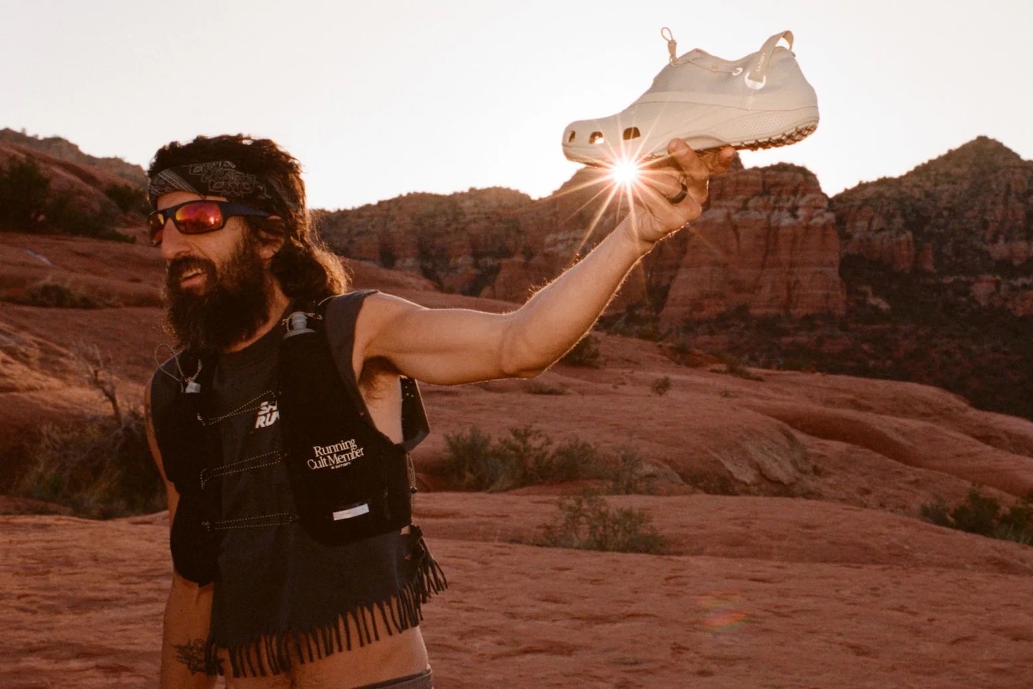 a runner in the desert holding a pair of the white Satisfy Crocs