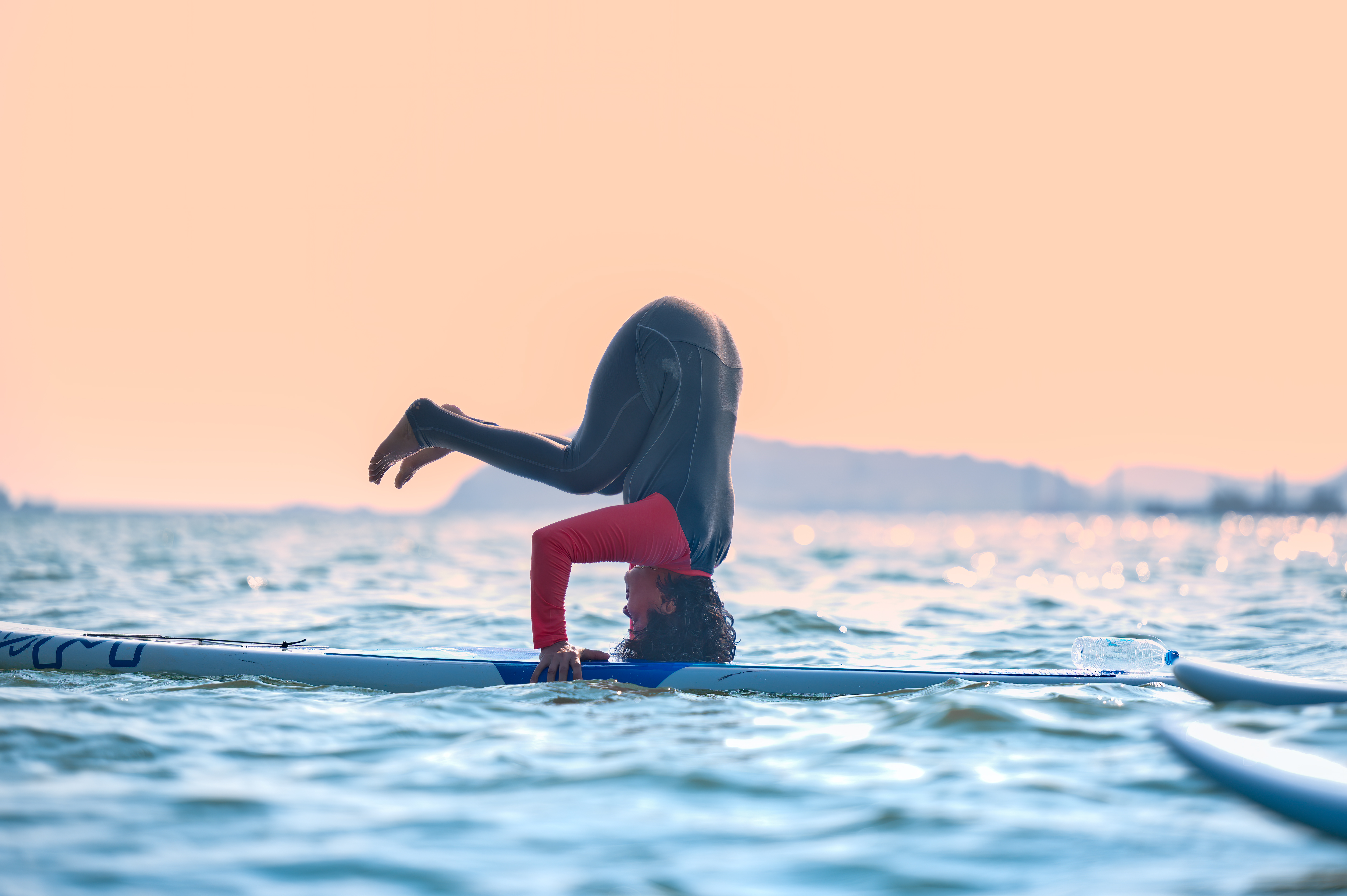 Un surfista de pie hace yoga en la tabla al atardecer.