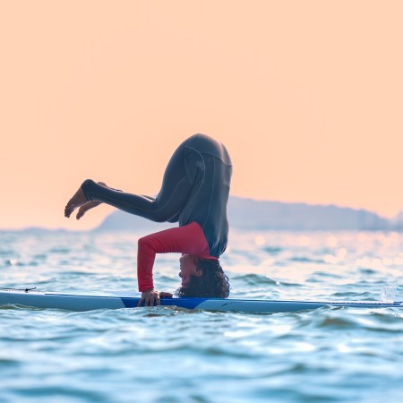 A stand-up apddleboarder does yoga on the board as the sun sets.