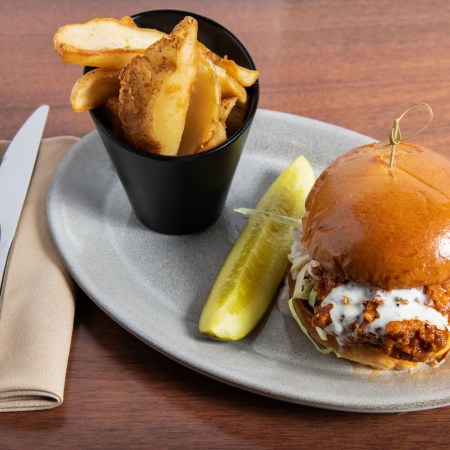 buffalo chicken sandwich on a plate with a pickle and cup of fries.