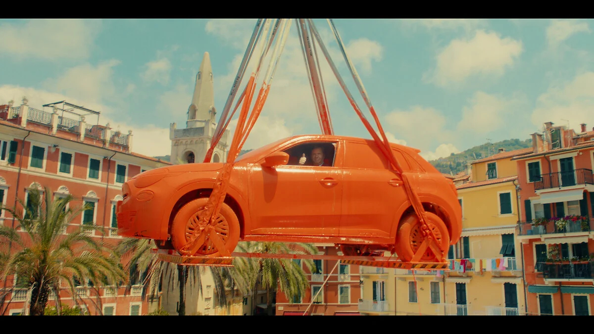 A Fiat completely dipped in orange paint emerges from a gray tank by crane