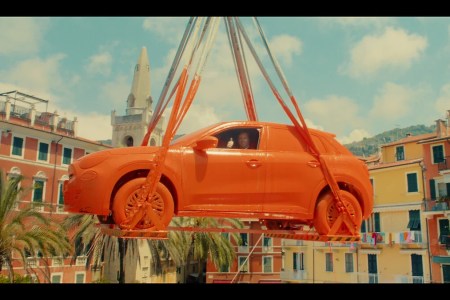 A Fiat completely dipped in orange paint emerges from a gray tank by crane