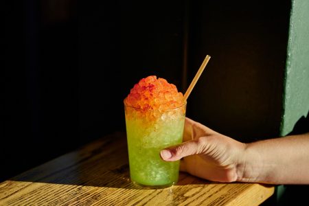 green slush-like cocktail with red on top and someone holding the cup