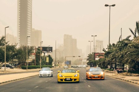 Three Porsche cars driving on road.