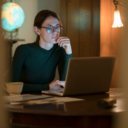 professional woman working in her home study at night with a laptop on the table