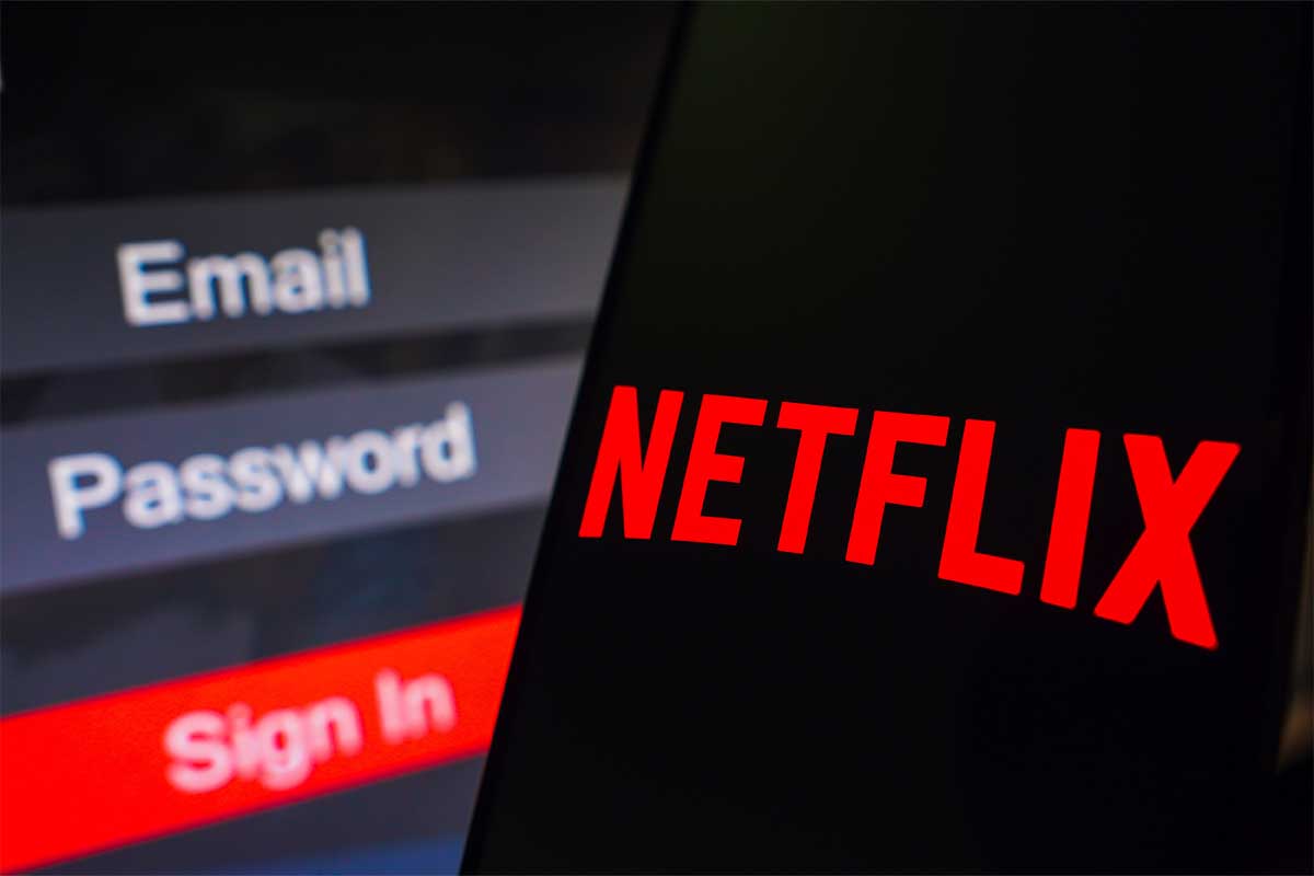 In this photo illustration, the Netflix logo is displayed on a smartphone screen, next to a login screen, with email, password, and sign in.