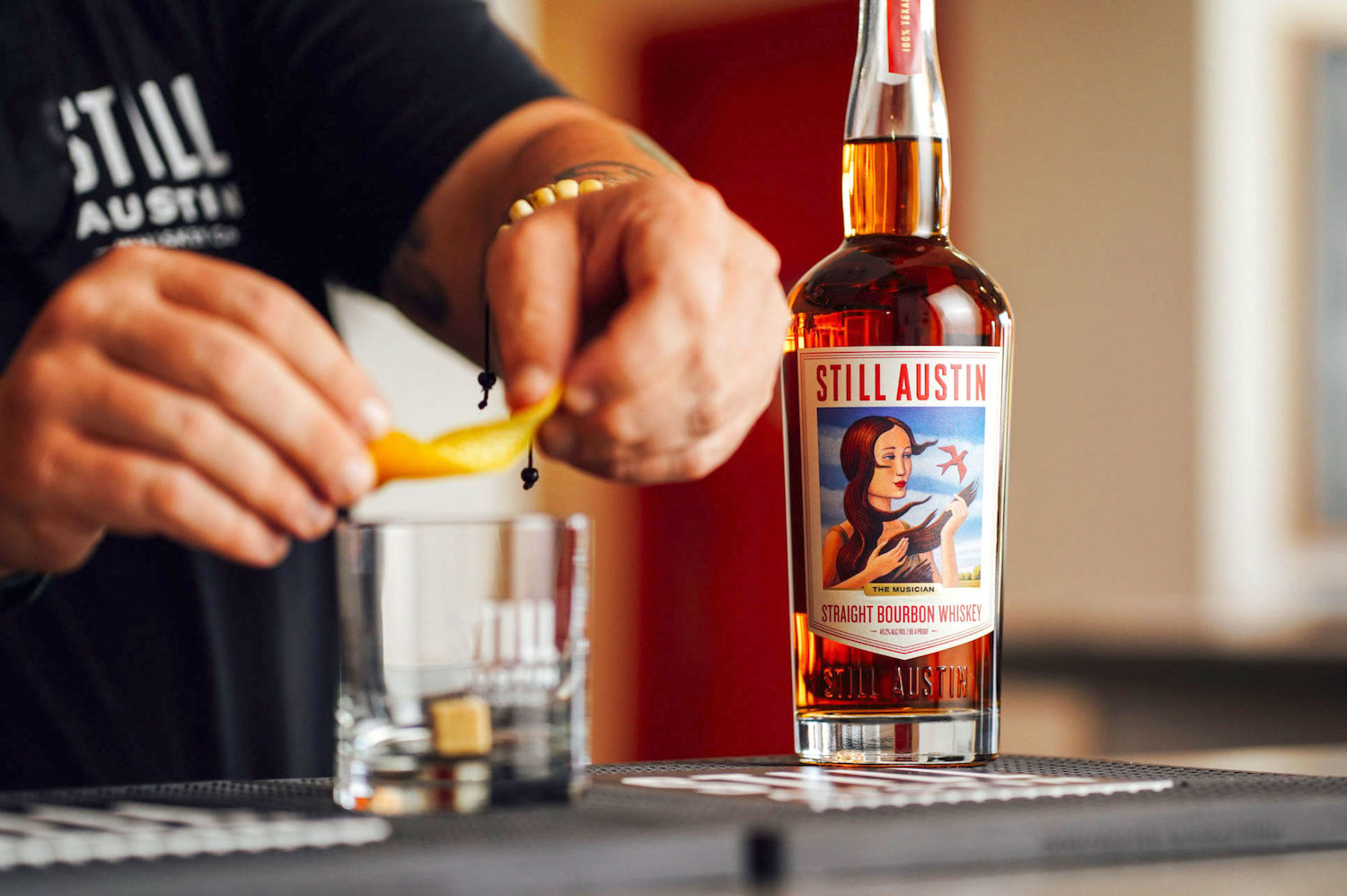 hands rimming a glass with lemon peel next to a bottle of whiskey