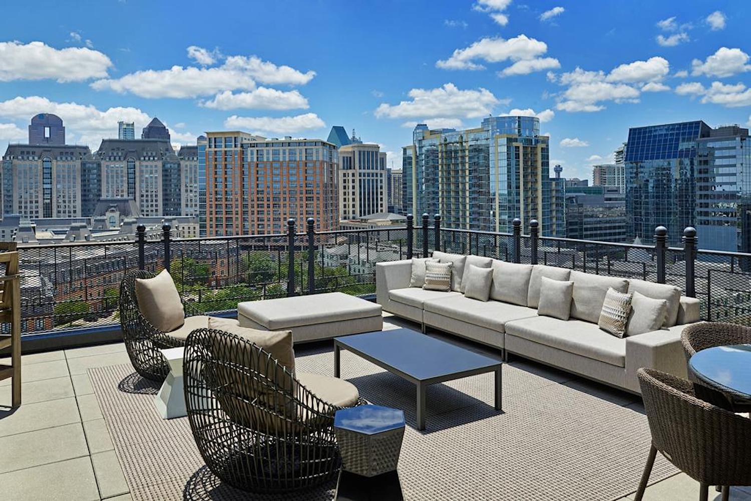 a rooftop deck with couches and tables overlooking a city.