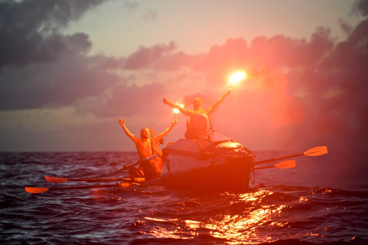 A group of men in a rowboat in the Atlantic, holding flares.