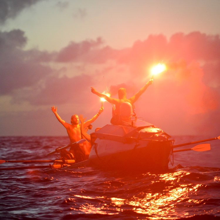 A group of men in a rowboat in the Atlantic, holding flares.