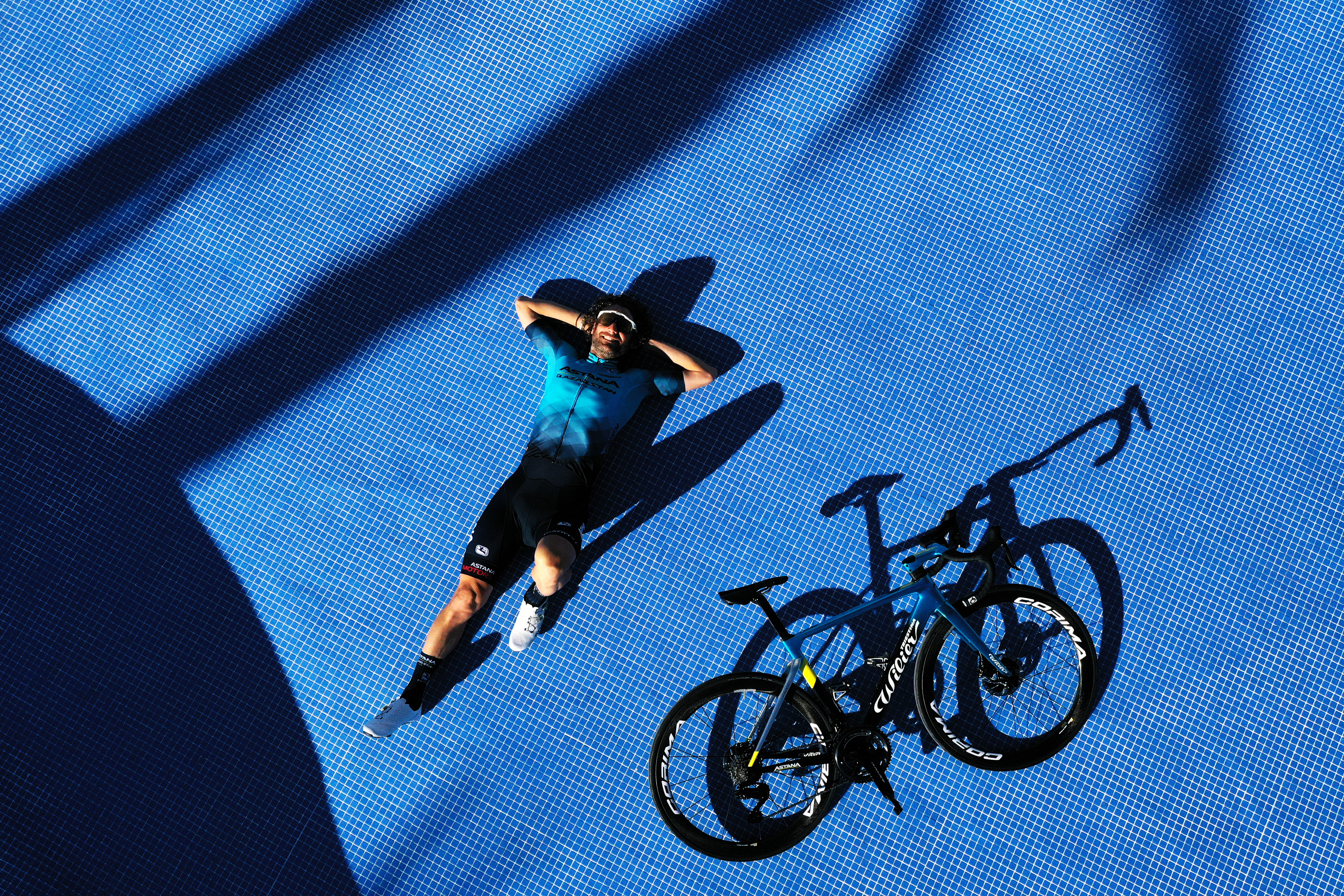 A biker takes a break, laying next to his bike on the ground.