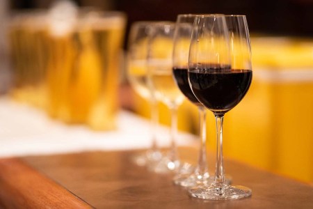 A glass of wine in front of several chilled beer glasses on a bar counter. For beer lovers, finding the right wine is an interesting exercise with unexpected results.