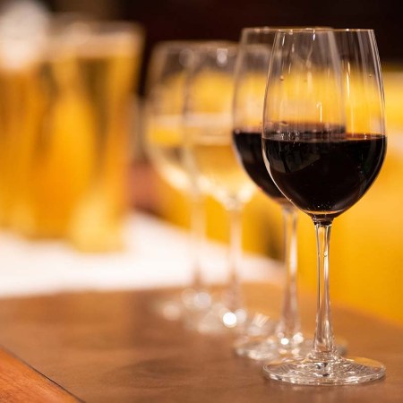 A glass of wine in front of several chilled beer glasses on a bar counter. For beer lovers, finding the right wine is an interesting exercise with unexpected results.