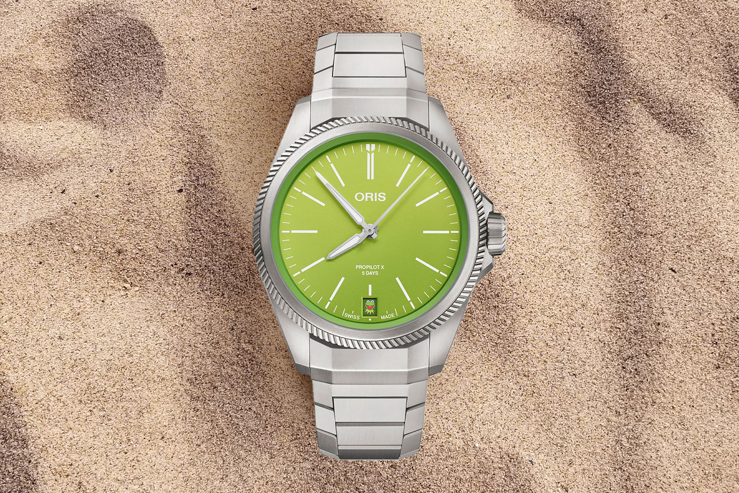 Silver watch with green face in the sand.