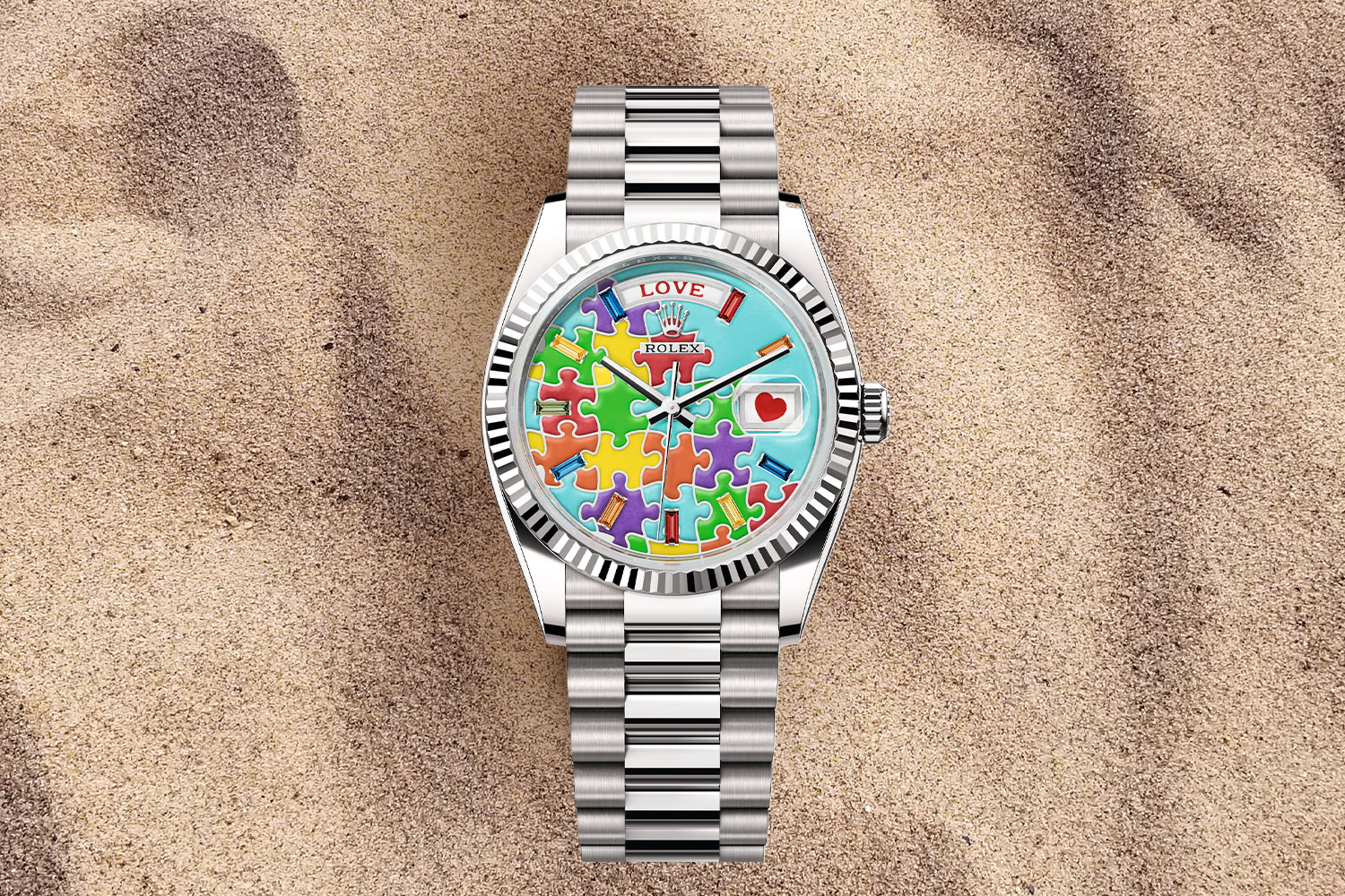Silver watch with blue face and multi-colored puzzle pieces on it in the sand.