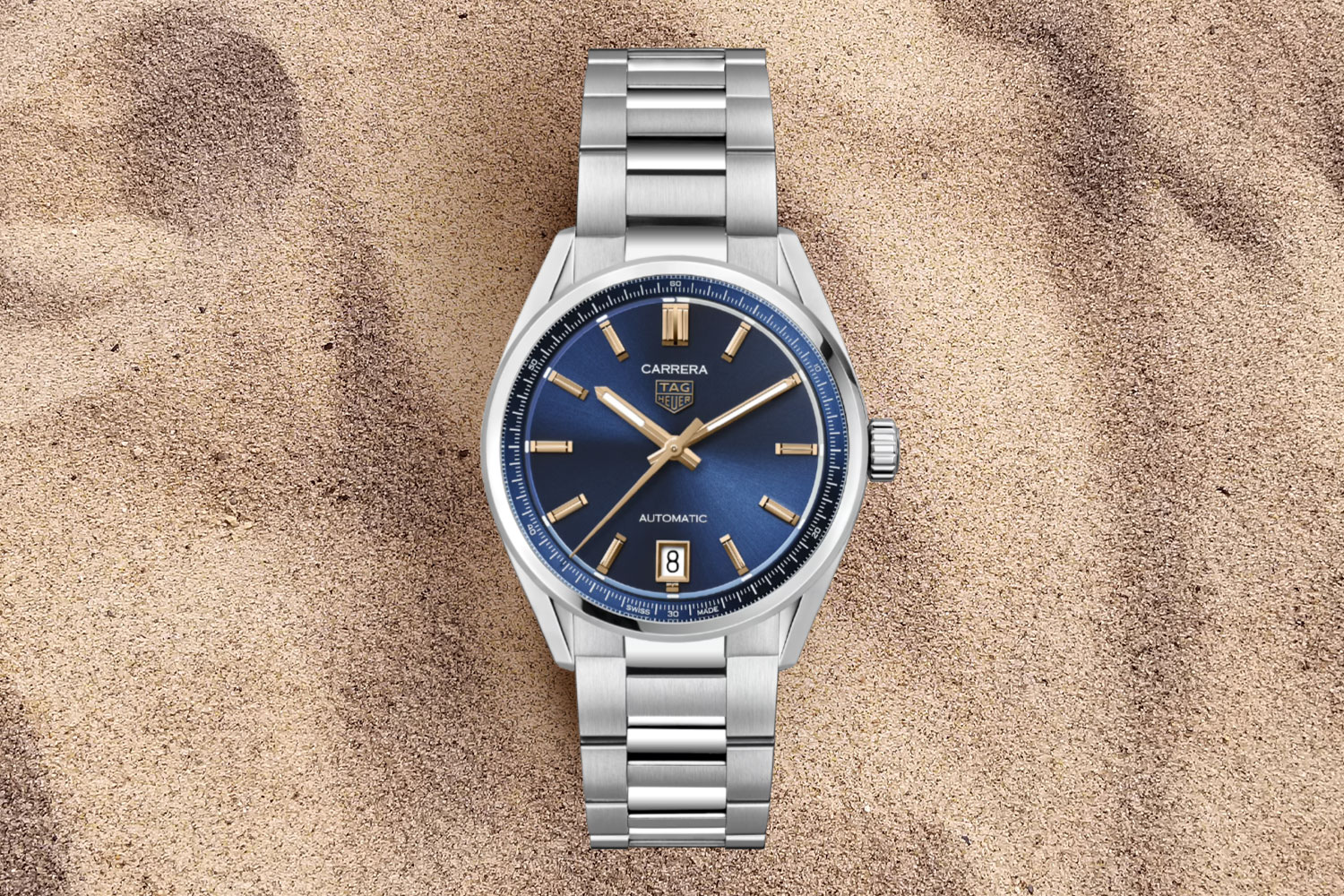 silver watch with blue face in the sand.