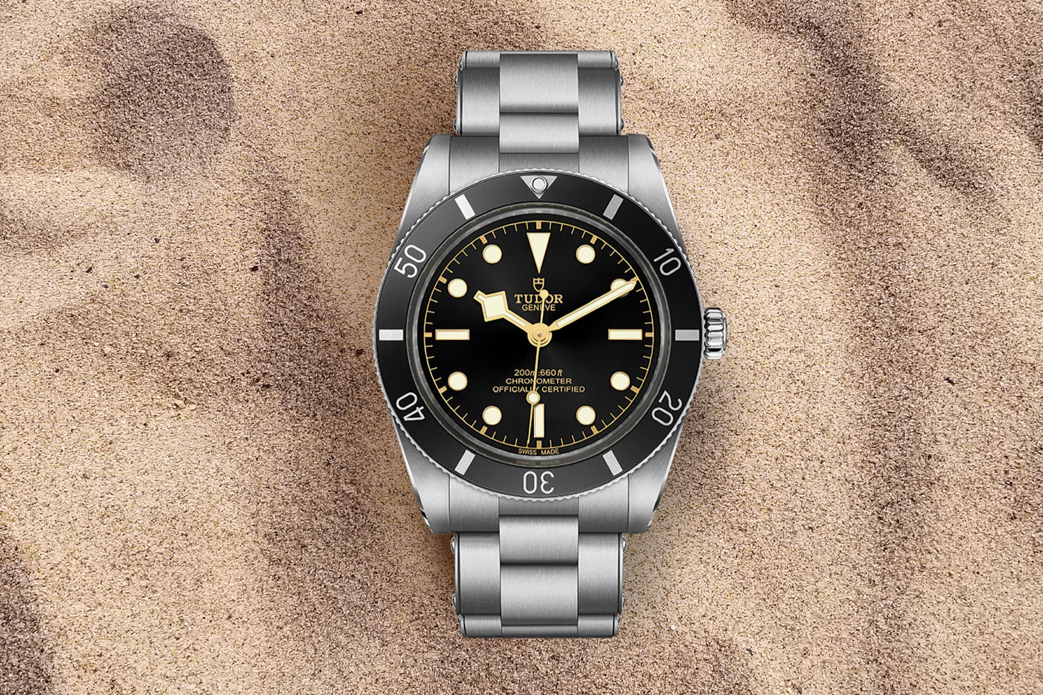 silver watch with black face and gold arrow hands in the sand.