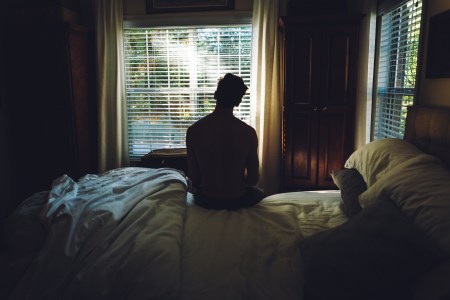 A man sitting on his bed staring out the window.