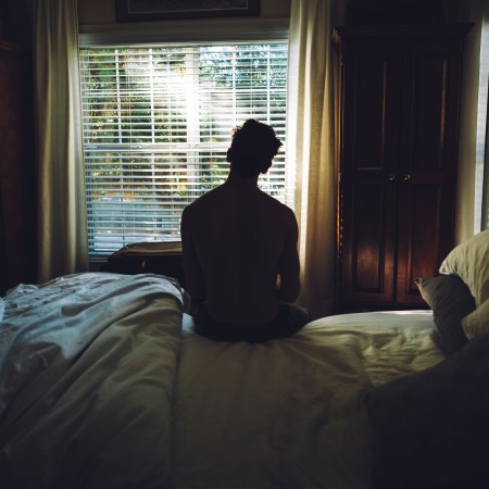 A man sitting on his bed staring out the window.