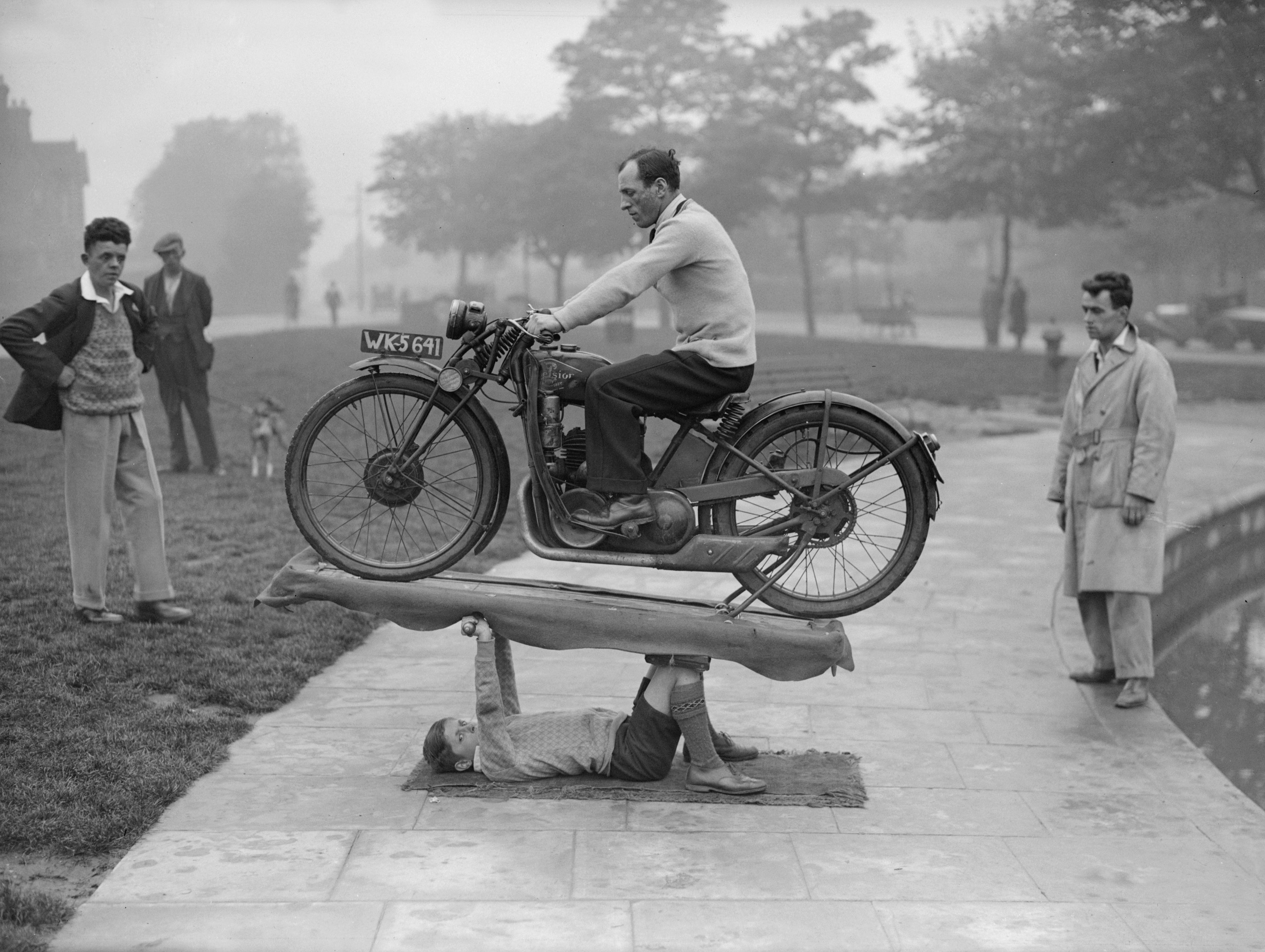 A kid lifting a man on a motorbike in a black-and-white tint.