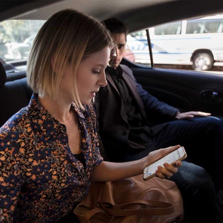 Man and woman sitting in car looking at phone. Uber has announced video ads are coming to its apps and even on tablets in its cars.