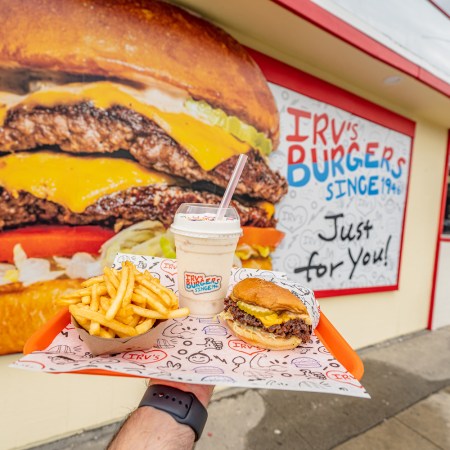 Burger, fries and a milkshake on a tray in front of a wall with a painted burger on it.