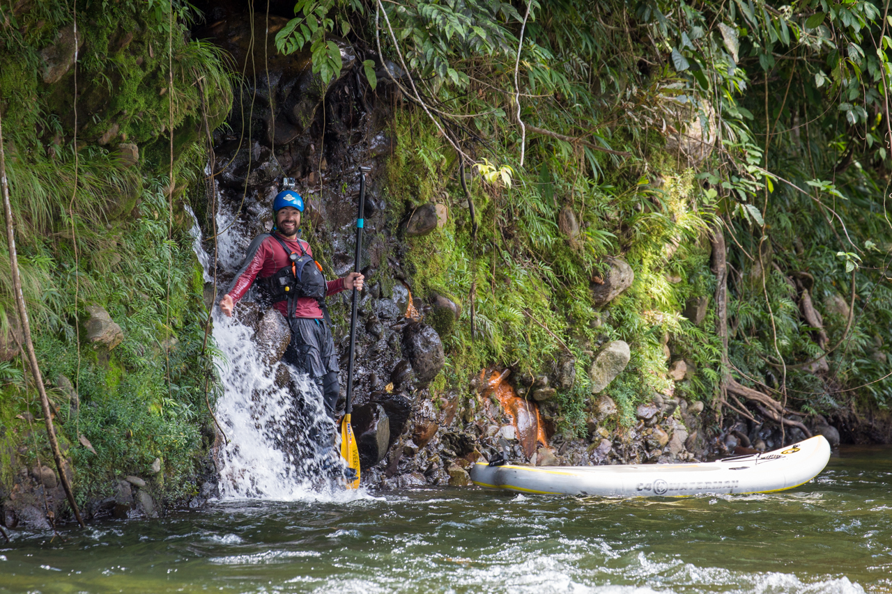 A paddleboarder smiles while being splashed by a small waterfall on the banks of the Madre de Dios river in Peru