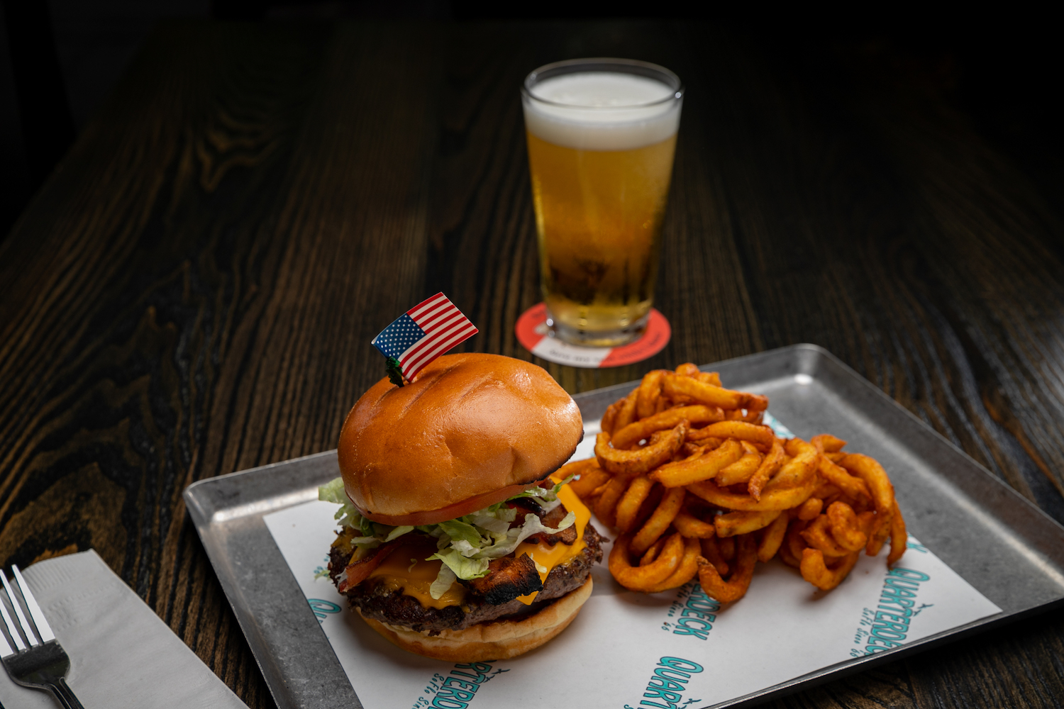 burger with an American flag poking out of the bun with fries and a beer.