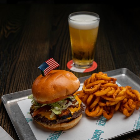 burger with an American flag poking out of the bun with fries and a beer.
