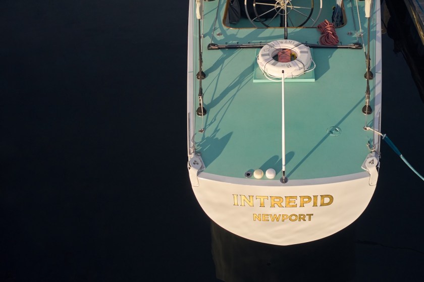 Teal and white boat with label "THE INTERPRID" in gold lettering on the top sailing across blue water.