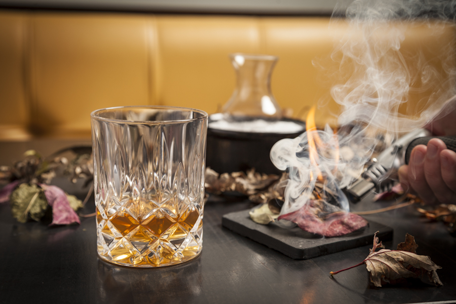 Whiskey glass partially filled with meat being smoked in the background.