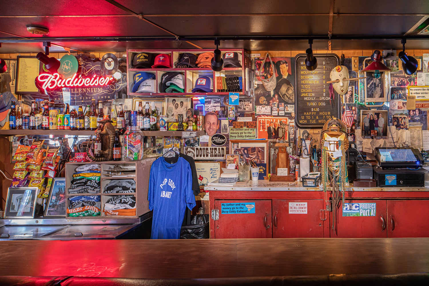 Posters, hats, merchandise, sweaters and food hung up along the wall behind a bar.