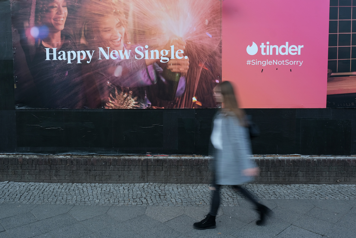 A young woman walks past a billboard advertisement for the dating app Tinder