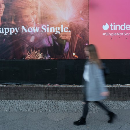 A young woman walks past a billboard advertisement for the dating app Tinder