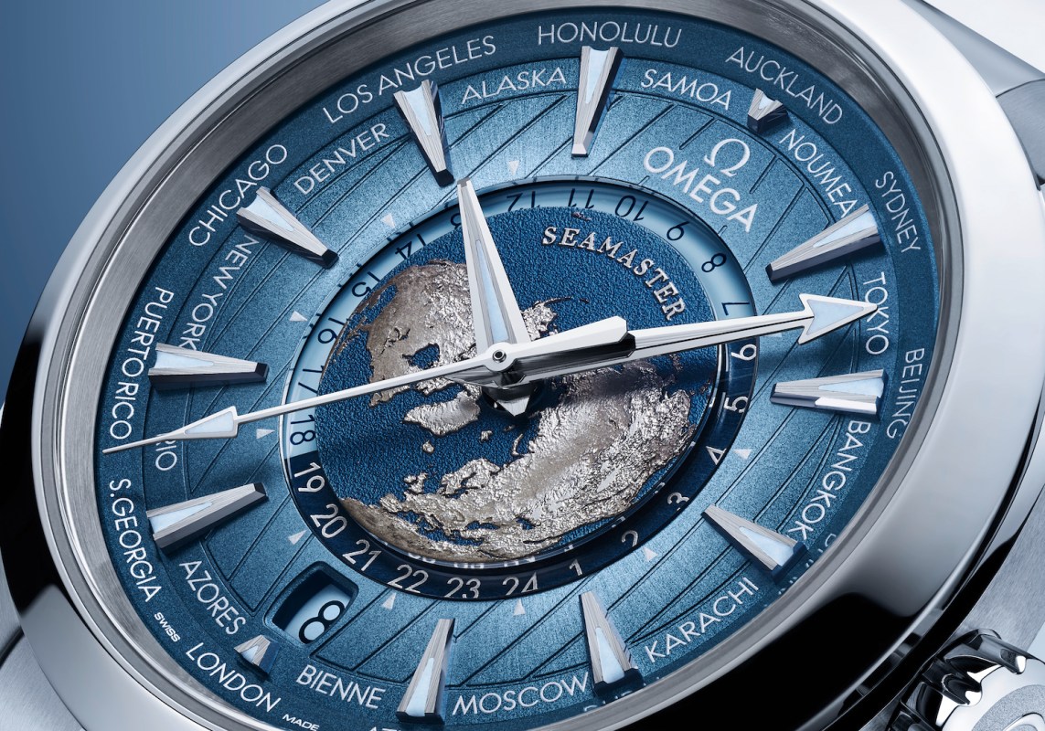 Up-close shot of a watch face that's blue with silver outlines of continents against a darker blue sphere, resembling Earth.